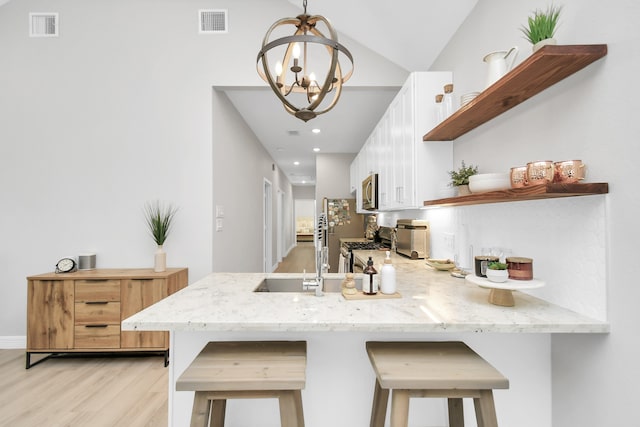 kitchen with kitchen peninsula, hanging light fixtures, a breakfast bar, white cabinetry, and light hardwood / wood-style floors