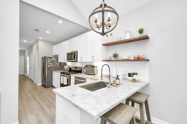 kitchen featuring kitchen peninsula, hanging light fixtures, a breakfast bar area, appliances with stainless steel finishes, and light hardwood / wood-style flooring