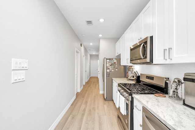 kitchen with white cabinets, light stone countertops, stainless steel appliances, and light wood-type flooring