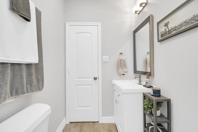 half bath featuring toilet, vanity, wood finished floors, and baseboards