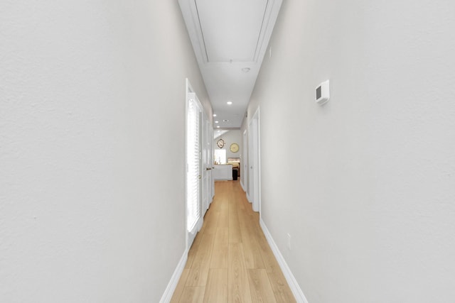 hallway featuring attic access, light wood-style floors, recessed lighting, and baseboards