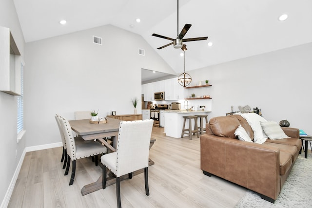 dining space with light hardwood / wood-style floors, sink, high vaulted ceiling, and ceiling fan with notable chandelier