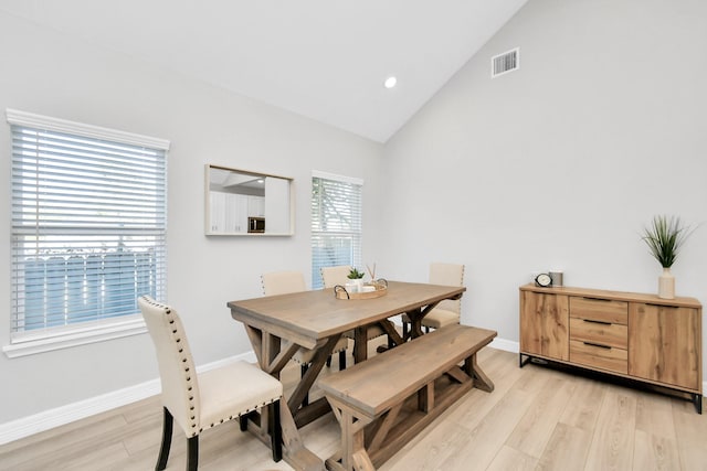 dining space with light wood-style floors, high vaulted ceiling, visible vents, and baseboards