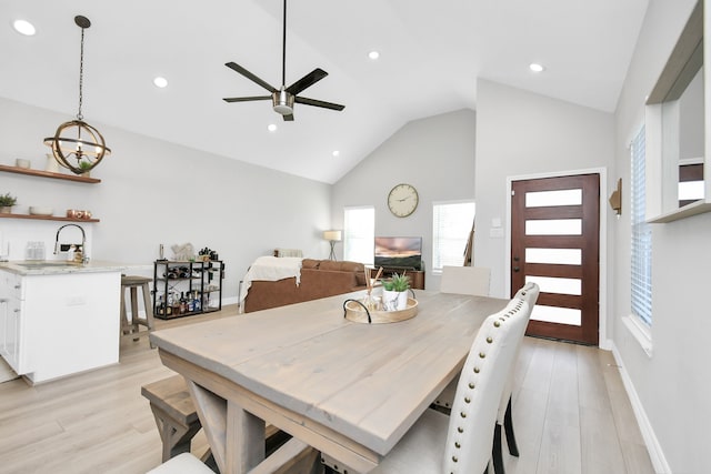 dining room with sink, high vaulted ceiling, light hardwood / wood-style flooring, and ceiling fan with notable chandelier