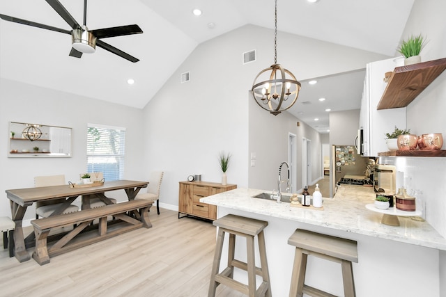 kitchen featuring a kitchen breakfast bar, light hardwood / wood-style flooring, hanging light fixtures, light stone countertops, and high vaulted ceiling