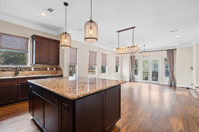 kitchen with a kitchen island, decorative light fixtures, sink, light stone countertops, and dark brown cabinets