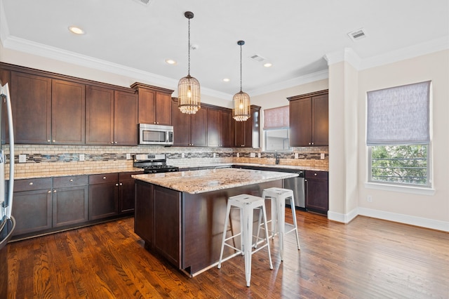 kitchen featuring a kitchen island, decorative light fixtures, stainless steel appliances, crown molding, and light stone countertops