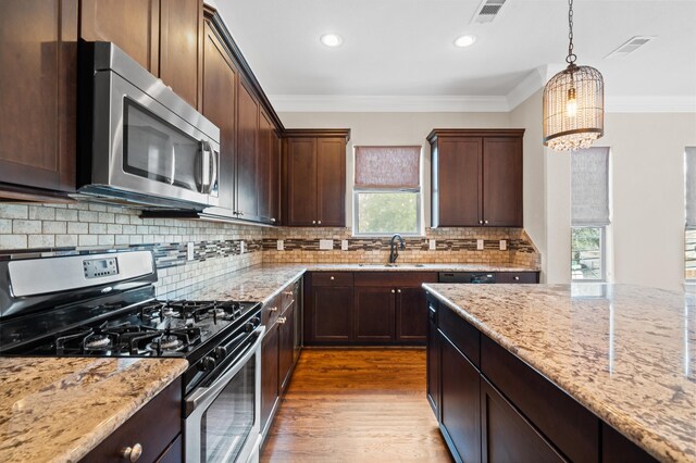 kitchen featuring sink, appliances with stainless steel finishes, hanging light fixtures, ornamental molding, and light stone countertops