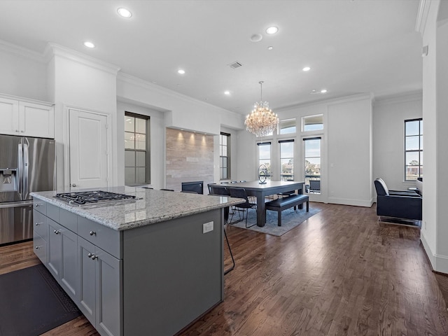 kitchen with ornamental molding, dark wood-type flooring, a center island, stainless steel appliances, and a notable chandelier