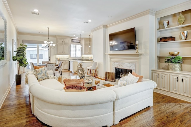 living room with crown molding, a chandelier, a fireplace, and wood-type flooring