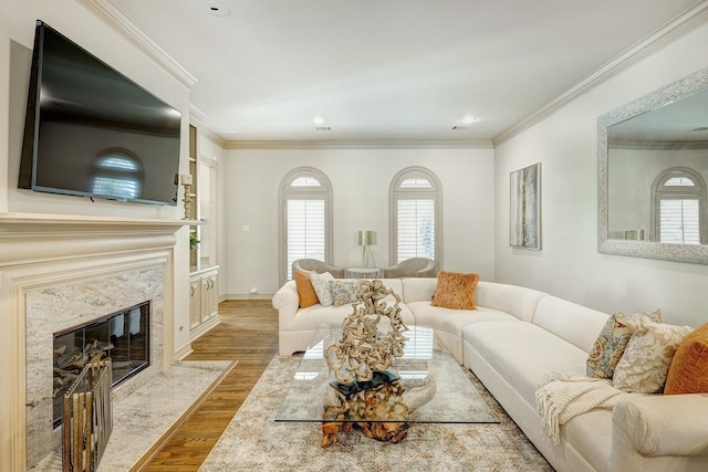 living room featuring a high end fireplace, ornamental molding, and light wood-type flooring