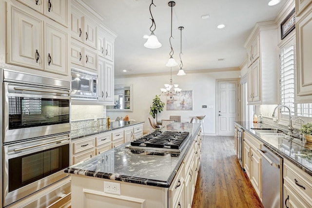 kitchen featuring appliances with stainless steel finishes, sink, decorative light fixtures, dark stone countertops, and a center island