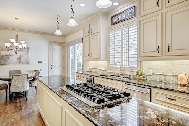 kitchen featuring appliances with stainless steel finishes, sink, cream cabinets, decorative light fixtures, and dark stone countertops