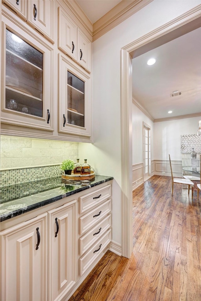 bar featuring light hardwood / wood-style flooring, dark stone counters, and cream cabinetry