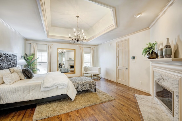 bedroom featuring an inviting chandelier, a high end fireplace, crown molding, hardwood / wood-style floors, and a tray ceiling