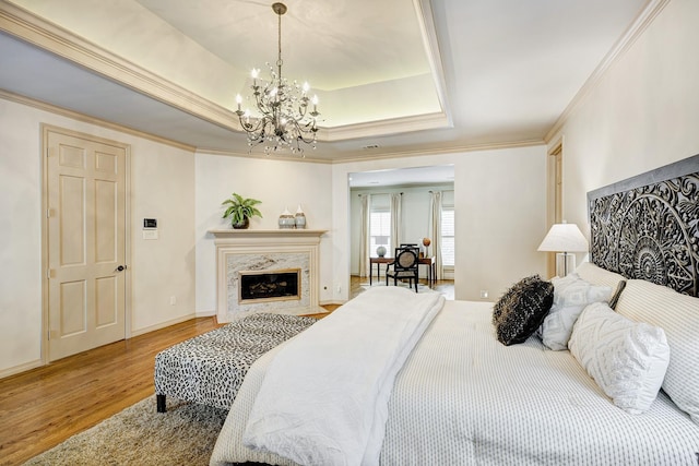 bedroom featuring a high end fireplace, a raised ceiling, crown molding, a notable chandelier, and hardwood / wood-style floors