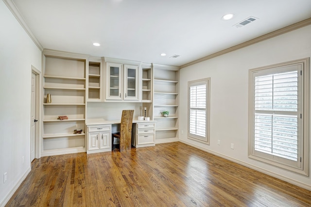 unfurnished office featuring built in features, built in desk, crown molding, and dark wood-type flooring