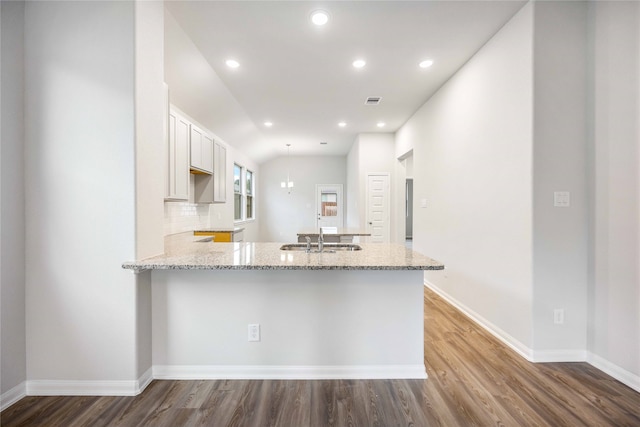 kitchen with kitchen peninsula, wood-type flooring, sink, light stone countertops, and white cabinets