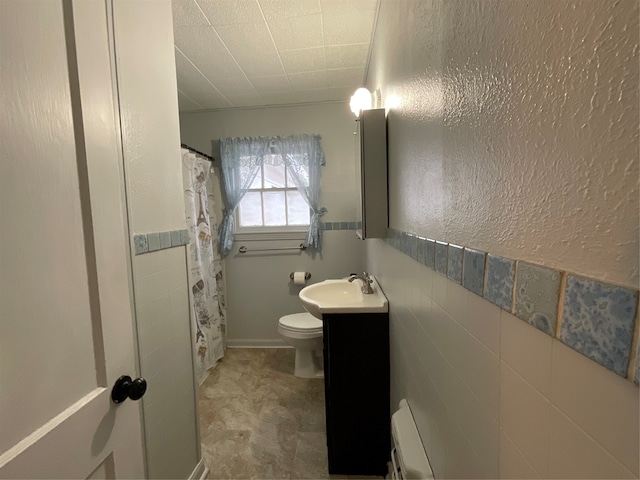 bathroom featuring vanity, toilet, tile walls, and a baseboard heating unit