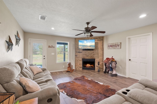 living room featuring ceiling fan, light hardwood / wood-style floors, a textured ceiling, and a brick fireplace