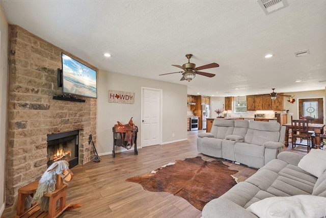 living room featuring a textured ceiling, ceiling fan, light hardwood / wood-style floors, and a fireplace