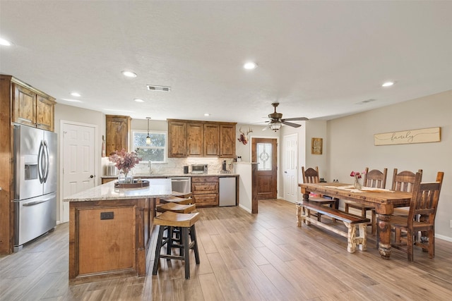 kitchen featuring a center island, backsplash, light stone countertops, light wood-type flooring, and stainless steel appliances