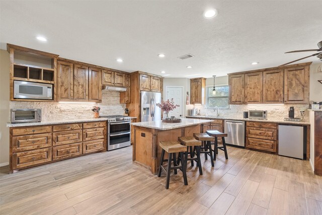 kitchen featuring appliances with stainless steel finishes, light wood-type flooring, decorative light fixtures, a kitchen island, and a breakfast bar area