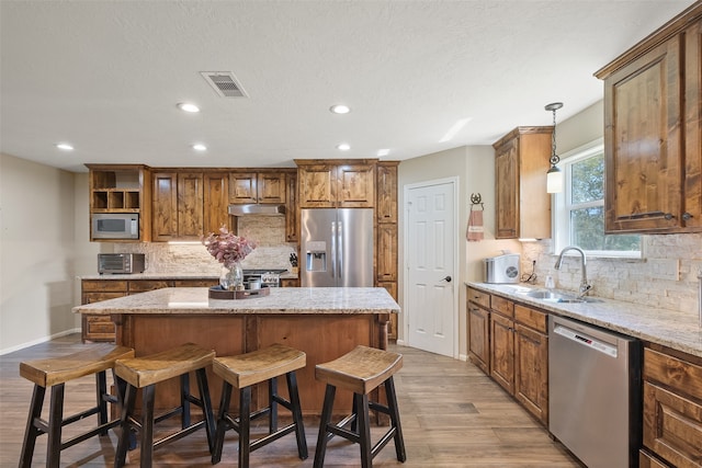 kitchen featuring light stone countertops, sink, a center island, hanging light fixtures, and appliances with stainless steel finishes