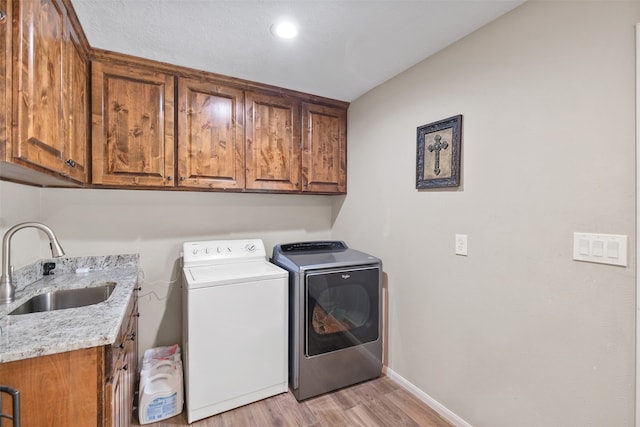 laundry area with cabinets, light wood-type flooring, sink, and washing machine and clothes dryer