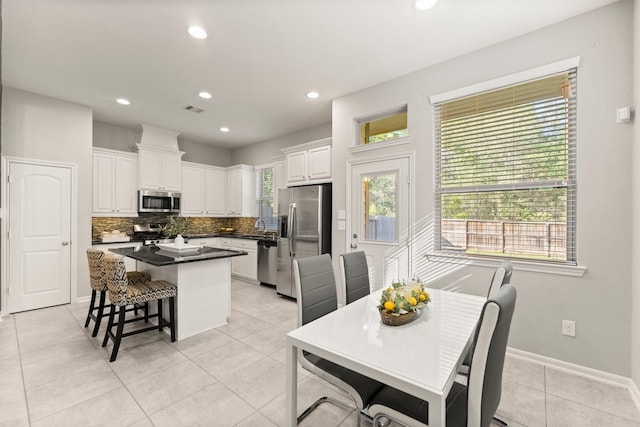 kitchen with a kitchen island, tasteful backsplash, white cabinetry, light tile patterned floors, and stainless steel appliances