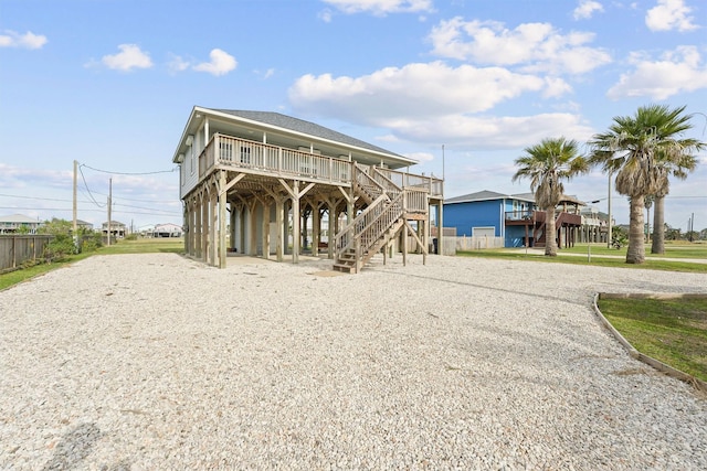 beach home featuring a carport, a wooden deck, gravel driveway, fence, and stairway