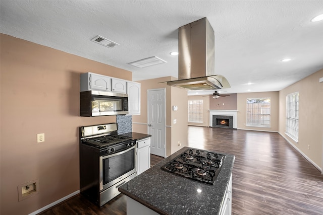 kitchen with island exhaust hood, white cabinetry, appliances with stainless steel finishes, a textured ceiling, and dark hardwood / wood-style flooring