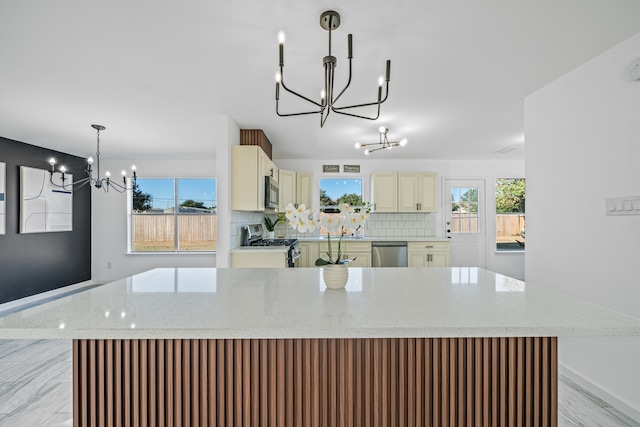 kitchen with appliances with stainless steel finishes, a healthy amount of sunlight, hanging light fixtures, and cream cabinetry