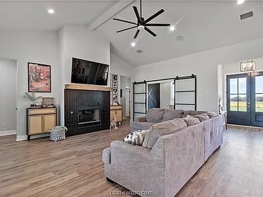 living room featuring high vaulted ceiling, a barn door, french doors, ceiling fan, and hardwood / wood-style flooring