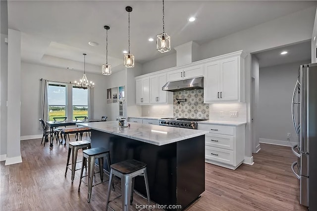 kitchen featuring white cabinets, appliances with stainless steel finishes, a kitchen island with sink, wood-type flooring, and pendant lighting