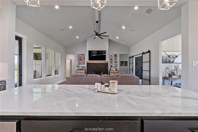 kitchen with a center island, a barn door, light stone counters, and lofted ceiling with beams