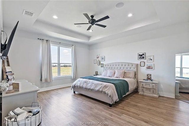 bedroom featuring ceiling fan, a tray ceiling, and light hardwood / wood-style flooring