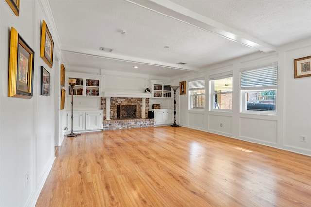 unfurnished living room with a textured ceiling, light hardwood / wood-style floors, a fireplace, built in features, and beamed ceiling