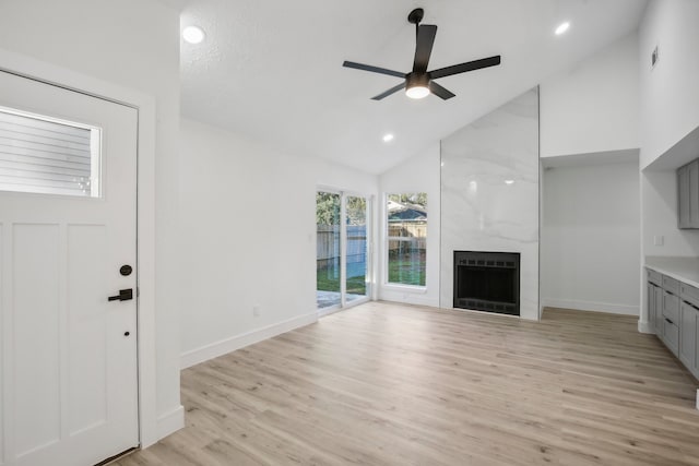 unfurnished living room featuring a large fireplace, light hardwood / wood-style floors, high vaulted ceiling, and ceiling fan