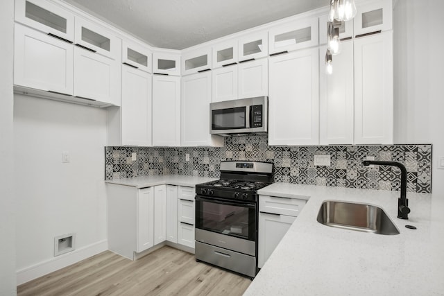 kitchen with sink, light wood-type flooring, white cabinetry, stainless steel appliances, and pendant lighting