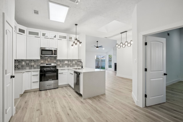 kitchen featuring lofted ceiling, kitchen peninsula, white cabinets, decorative light fixtures, and appliances with stainless steel finishes