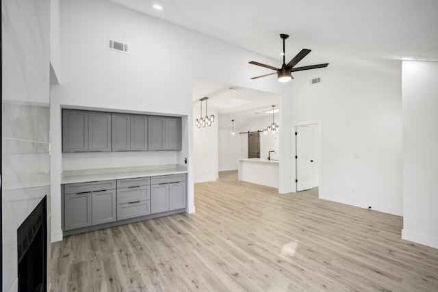 unfurnished living room featuring a towering ceiling, light hardwood / wood-style flooring, and ceiling fan with notable chandelier