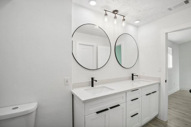 bathroom with vanity, toilet, wood-type flooring, and a textured ceiling