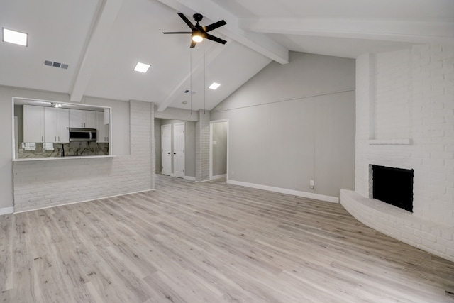 unfurnished living room with beamed ceiling, light hardwood / wood-style flooring, a brick fireplace, and ceiling fan