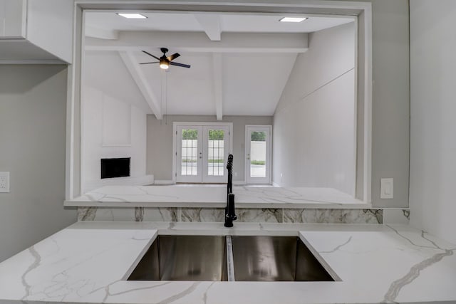 kitchen featuring sink, lofted ceiling with beams, light stone counters, and ceiling fan