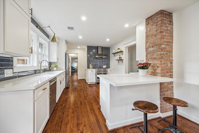 kitchen featuring white cabinets, a kitchen bar, sink, and wall chimney range hood