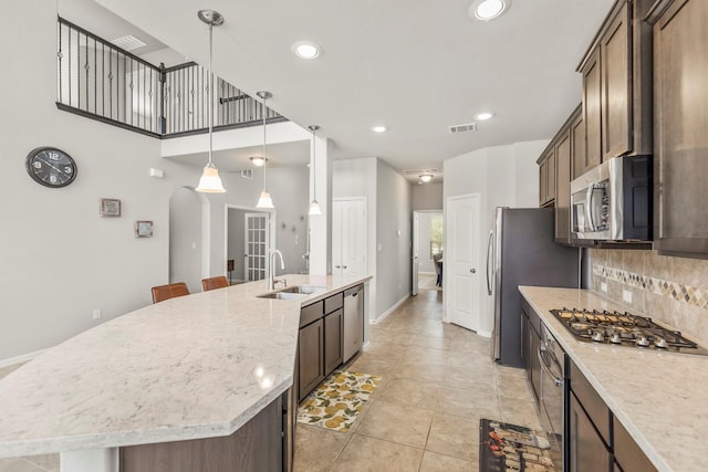 kitchen featuring an island with sink, sink, decorative light fixtures, appliances with stainless steel finishes, and light stone counters