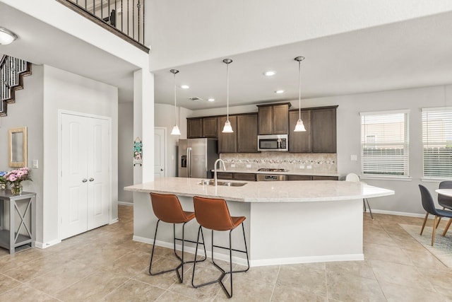 kitchen featuring a center island with sink, light stone counters, backsplash, appliances with stainless steel finishes, and sink