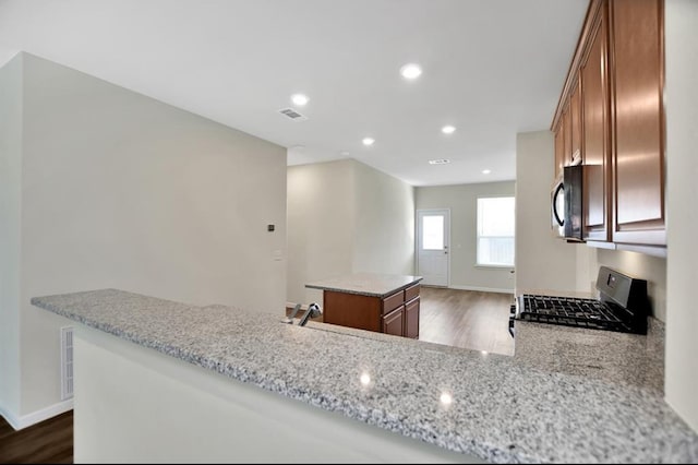 kitchen with light stone counters, kitchen peninsula, stove, and dark hardwood / wood-style floors