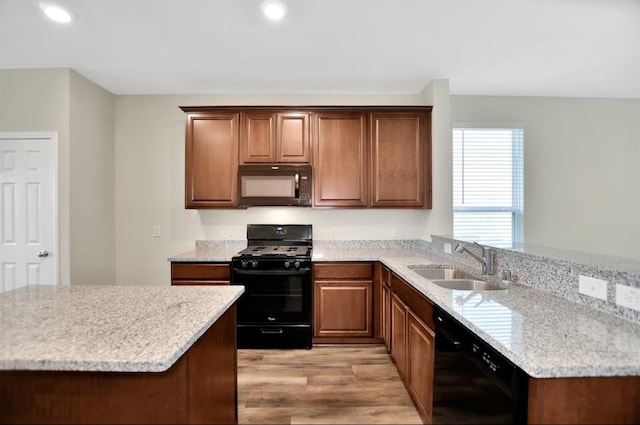 kitchen with kitchen peninsula, light stone counters, light hardwood / wood-style flooring, black appliances, and sink